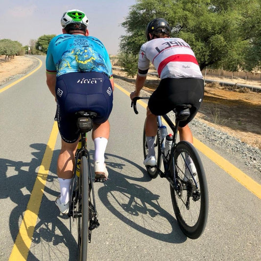 Two cyclists on the road wearing white cycling socks with a blue toe area, the socks reach mid-calf height.